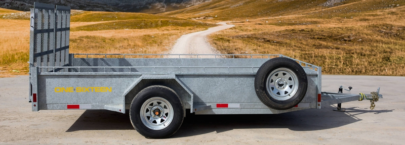 Galvanized One Sixteen tandem axle utility trailer with spare tire, designed for heavy-duty hauling, parked on a rural road – McFarlane Trailer Sales Ontario