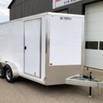 White enclosed utility trailer with dual axles and diamond-plate front, parked outside a building with ENBECK logo visible on the front corner panel