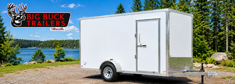 White enclosed trailer on a gravel lot by a lake and forest, with a Big Buck Trailers logo in the top-left corner.