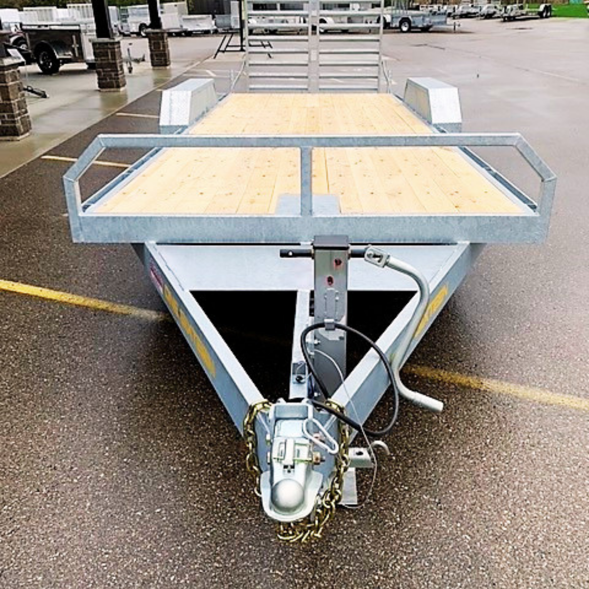 Front view of a metal utility trailer with a wooden deck and hitch, parked in a lot.