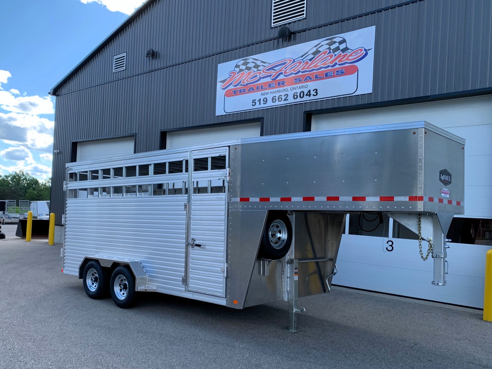 image1 58 - McFarlane Trailer Sales Silver multi-axle gooseneck trailer parked in front of a gray metal building with a large 'MC Haul Trailers Sales' sign above the doors