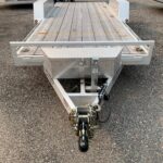 Front view of a aluminum utility trailer with a wooden deck and diamond-plate fenders on a gravel lot, with other trailers in the background.