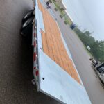 Flatbed trailer with wooden deck and diamond-plate sides in a parking lot at an industrial site.