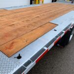 Flatbed trailer with a brown wooden deck and silver diamond-plate trim, parked on pavement.