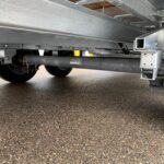 Underside view of a metal trailer frame showing wheels, beams, and hydraulic components; mudflap with a KTRAIL logo visible at left.