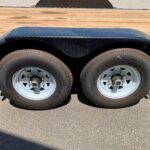 image2 48 - McFarlane Trailer Sales Dual-axle trailer with diamond-plate fenders over two tires and a wooden bed visible above the wheels, on a paved surface.