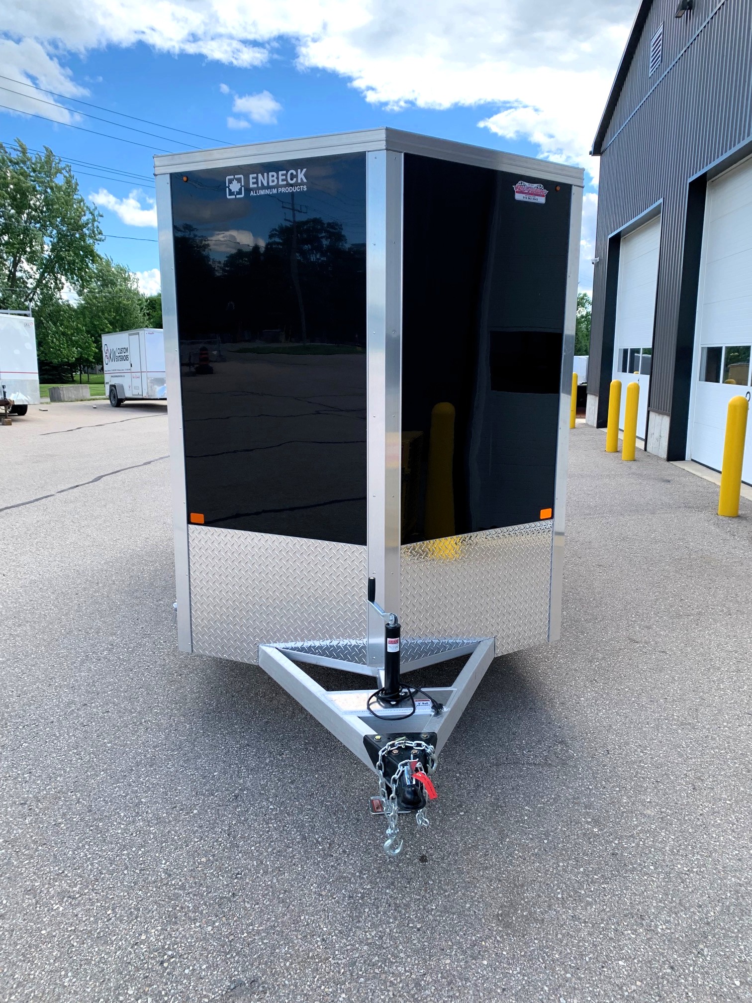 image2 51 - McFarlane Trailer Sales Black enclosed cargo trailer with aluminum framing and diamond-plate trim, hitched in an industrial lot.