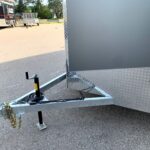 Close-up of a metal trailer with diamond-plate sides and a hitch resting on a paved lot, with chains and jack visible in the foreground.