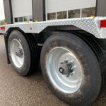 Close-up of a heavy-duty trailer wheel set with a diamond-plate fender, dual tires, hub assemblies, and orange reflectors.