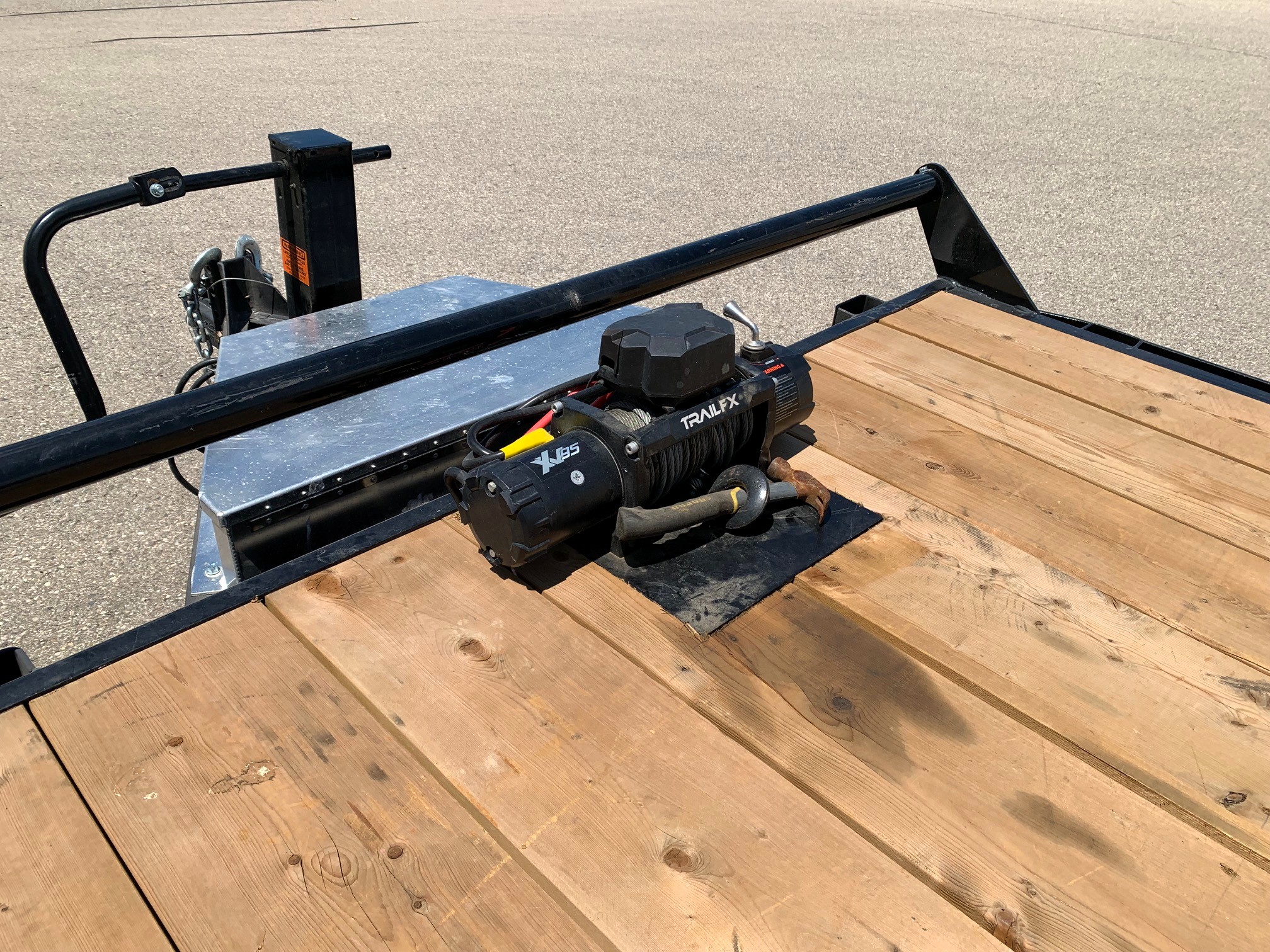 image3 44 - McFarlane Trailer Sales Flatbed trailer deck with a mounted electric winch and a protective rail, parked on pavement.