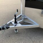image3 46 - McFarlane Trailer Sales Trailer hitch and jack assembly on a metal-framed trailer with diamond-plate siding and safety chains visible.