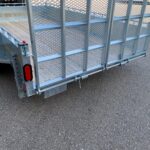 Rear view of a galvanized metal utility trailer with mesh sides, wooden bed, and red taillight on an asphalt lot.