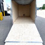 Empty enclosed cargo trailer with plywood walls and floor, ramp down on a paved lot, ready for loading.