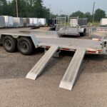 Row of aluminum cargo trailers parked in a gravel lot with trees behind them and utility poles in the distance.