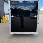 image6 28 - McFarlane Trailer Sales Rear view of a black enclosed trailer with silver frame and ENBECK Aluminum Products logo, reflecting a blue sky and clouds.