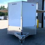 White enclosed utility trailer by a loading bay, featuring diamond-plate lower panel and hitch with safety chains in front