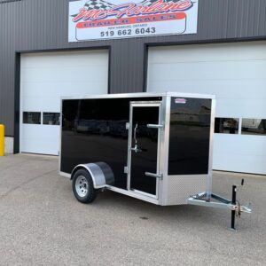 Black enclosed utility trailer with diamond-plate front parked in front of a grey industrial building with Roll-Up garage doors and a McAlline Trailers Sales sign above.