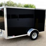 Black enclosed cargo trailer with silver trim and diamond-plate front, parked in a lot with trees in the background.