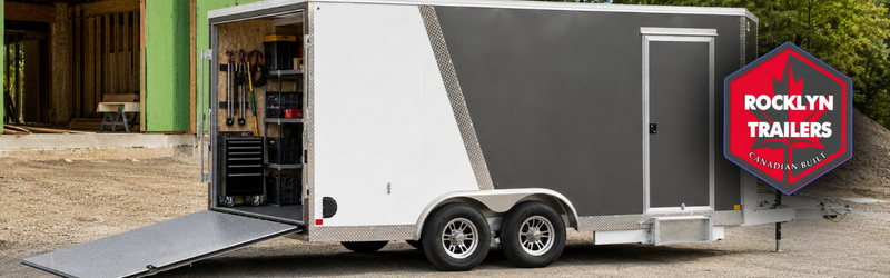 Enclosed dual-axle utility trailer on a dirt lot with rear ramp down; tool storage visible inside and Rocklyn Trailers logo on the side.