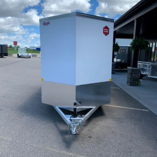 Enclosed utility trailer with a light-blue body and diamond-plate front, hitched to a tow bar, parked in a parking lot near a building under a blue sky with clouds.