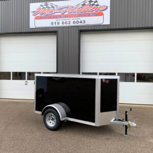 Black enclosed cargo trailer with a diamond-plate front, parked in front of a gray metal building with two white doors and a McLane Trailer Sales sign above.