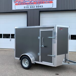 Grey enclosed utility trailer with diamond-plate front, parked in front of a trailer sales building.