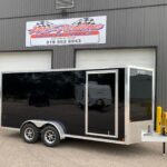 image1 60 - McFarlane Trailer Sales Black enclosed dual-axle cargo trailer with chrome trim and reflective sides, parked in front of a gray industrial building with a 'McAllane Trailer Sales' sign above.
