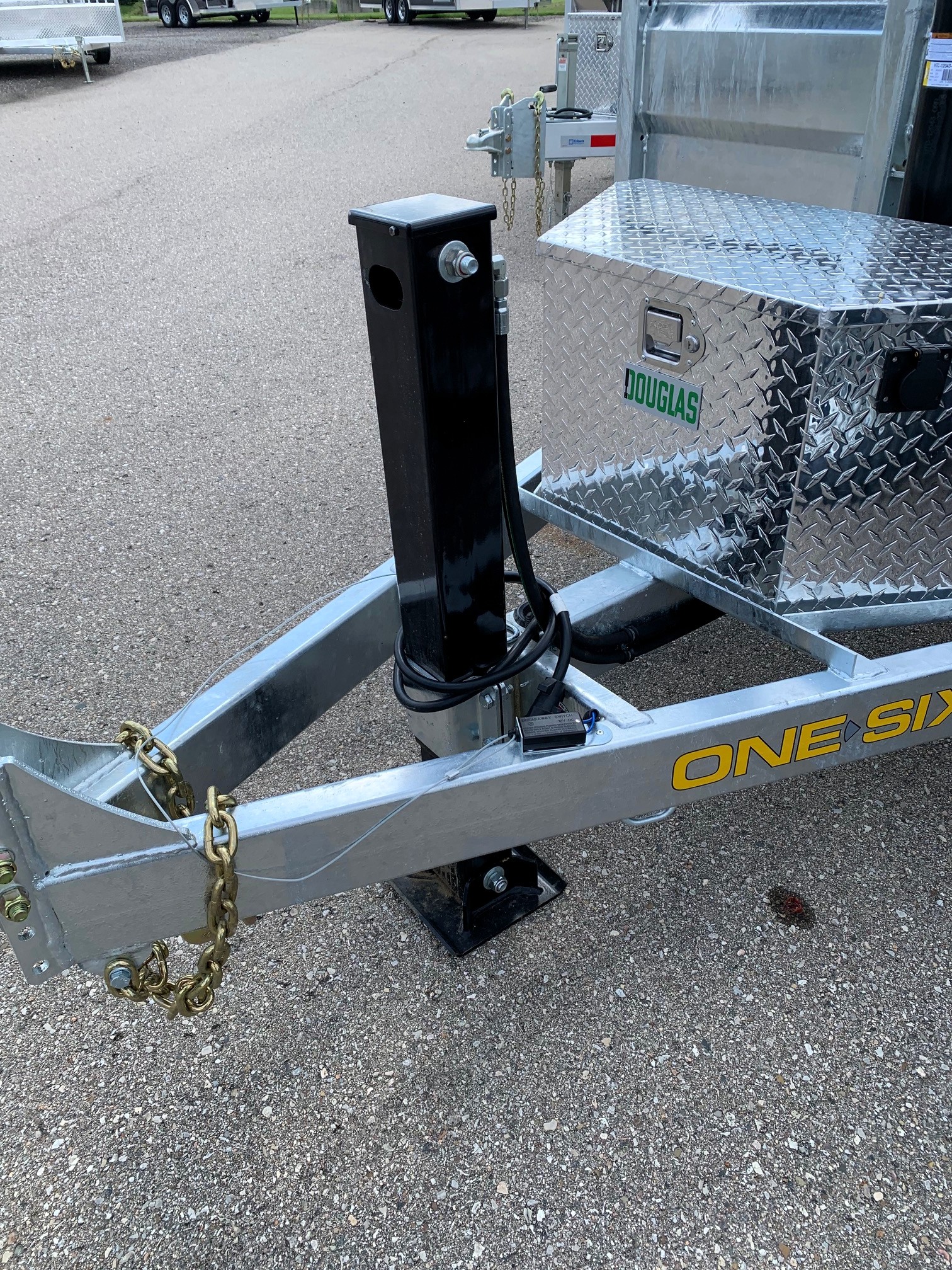 image1 62 - McFarlane Trailer Sales Trailer tongue with a black vertical jack post, safety chains, and a diamond-plate toolbox on a silver trailer labeled DOUGLAS.
