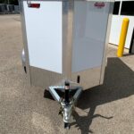 image2 58 - McFarlane Trailer Sales Front view of a silver enclosed utility trailer on a hitch, with diamond-plate at the base and safety chains; outdoors beside a white building.