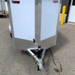Front view of a white enclosed trailer with metal trim and a hitch, parked outdoors on asphalt.