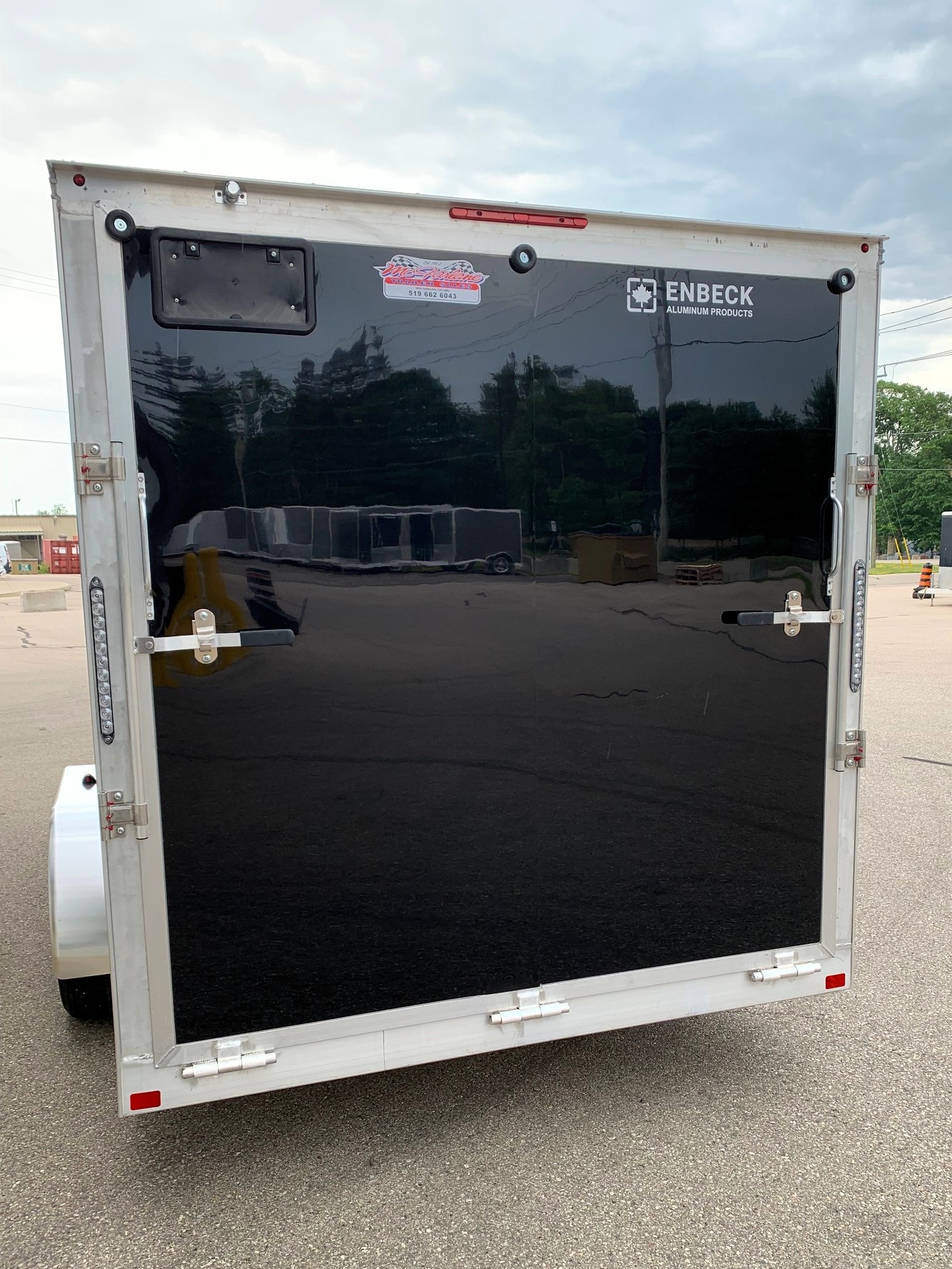 image4 51 - McFarlane Trailer Sales Rear view of a black enclosed trailer with silver aluminum frame and two doors, displaying ENBECK Aluminum Products logo sticker.