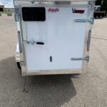 Rear view of a white enclosed trailer with diamond-plate trim, a small black window, and heavy-duty latches with two branding stickers nearby.