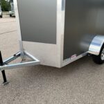 Close-up of a utility trailer hitch and front of a dark gray enclosed trailer with diamond plate trim and a wheel on the right side.