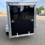 Rear view of a black enclosed trailer with diamond-plate trim, rear doors, and metal latches visible nearby a parking lot.