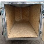 Open cargo trailer interior with plywood walls and diamond-plate exterior trim, empty for loading.