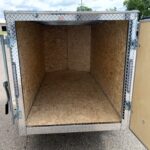 Empty cargo trailer interior with plywood walls and a diamond-plate exterior, rear doors swung open.
