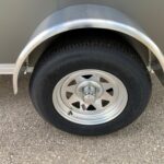 Close-up of a trailer wheel with silver fender and Goodyear tire on asphalt surface, showing lug nuts and hub area