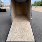 Empty enclosed trailer interior with plywood walls and a lowered wooden ramp at the rear.