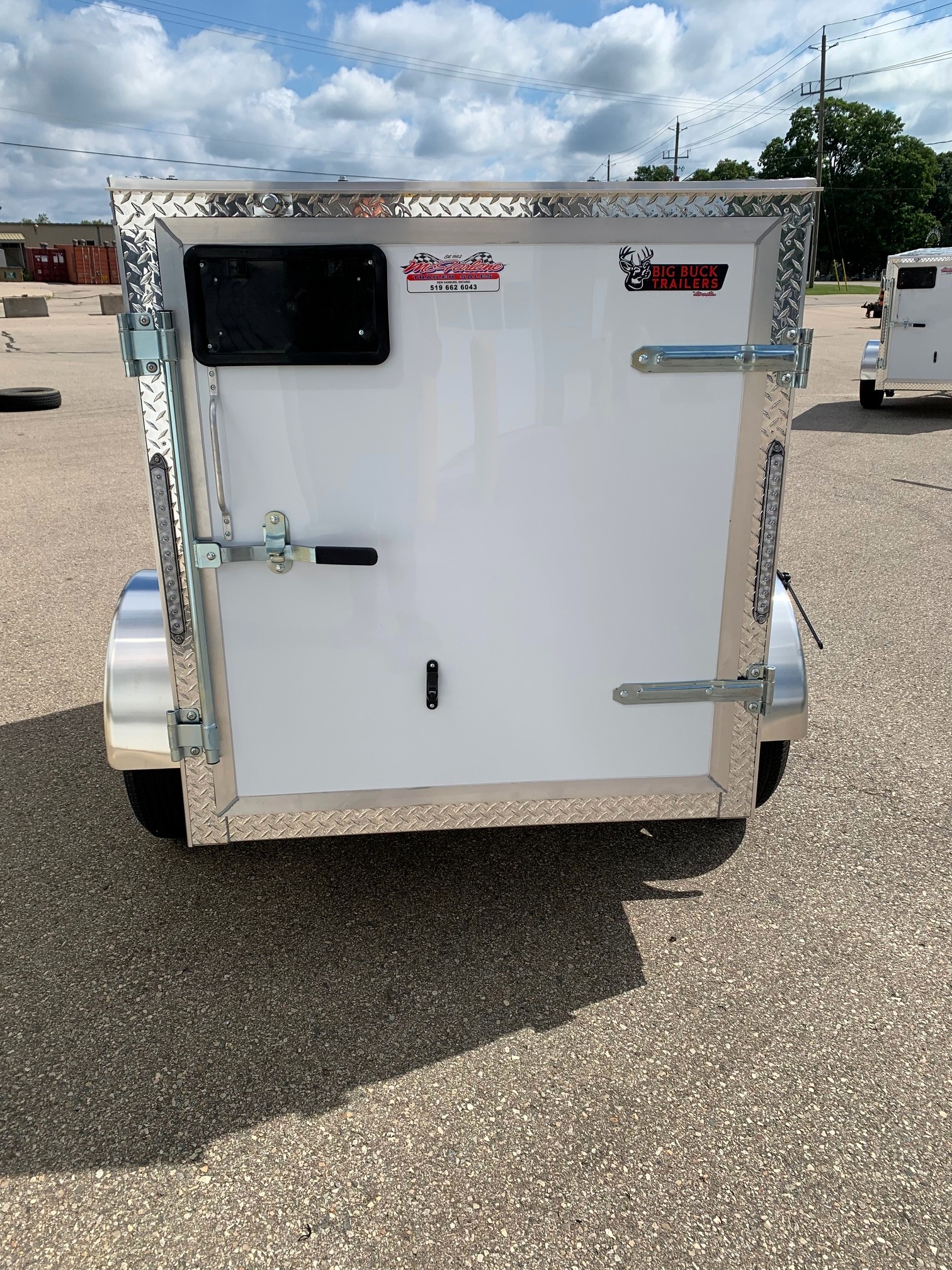 image6 35 - McFarlane Trailer Sales Rear of a white cargo trailer with diamond-plate trim, black window, and metal latches; stickers read 'Big Buck Trailers' and a small dealer label.