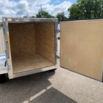 image7 27 - McFarlane Trailer Sales Open cargo trailer with plywood interior and diamond-plate trim along the edges in a parking lot, rear doors swung open.