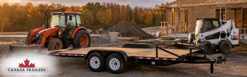Red tractor and Bobcat skid-steer on a construction site with a flatbed trailer, fall trees in the background.
