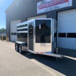image0 69 - McFarlane Trailer Sales Glossy black enclosed trailer with aluminum trim and diamond-plate accents, parked outside a service building with a large sign.