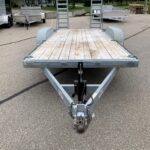 image0 70 - McFarlane Trailer Sales Flatbed utility trailer with a wooden deck and two raised ramps, parked in a lot with other trailers nearby.