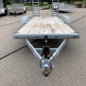 Flatbed utility trailer with a wooden deck and two raised ramps, parked in a lot with other trailers nearby.