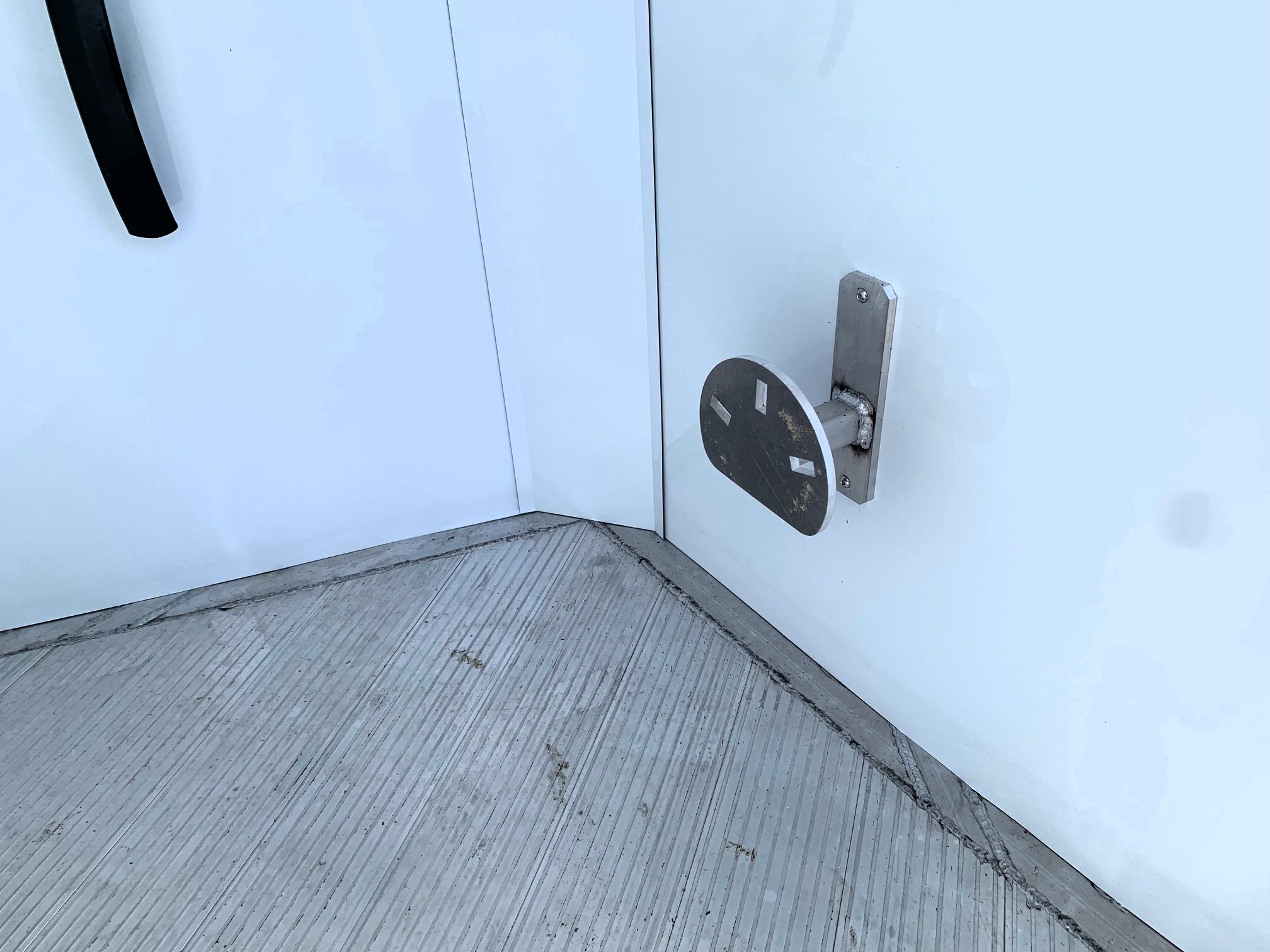 image10 8 - McFarlane Trailer Sales Close-up of a pale blue metal door showing a silver latch plate and mounting bracket on the right, with a dark curved handle on the left side.