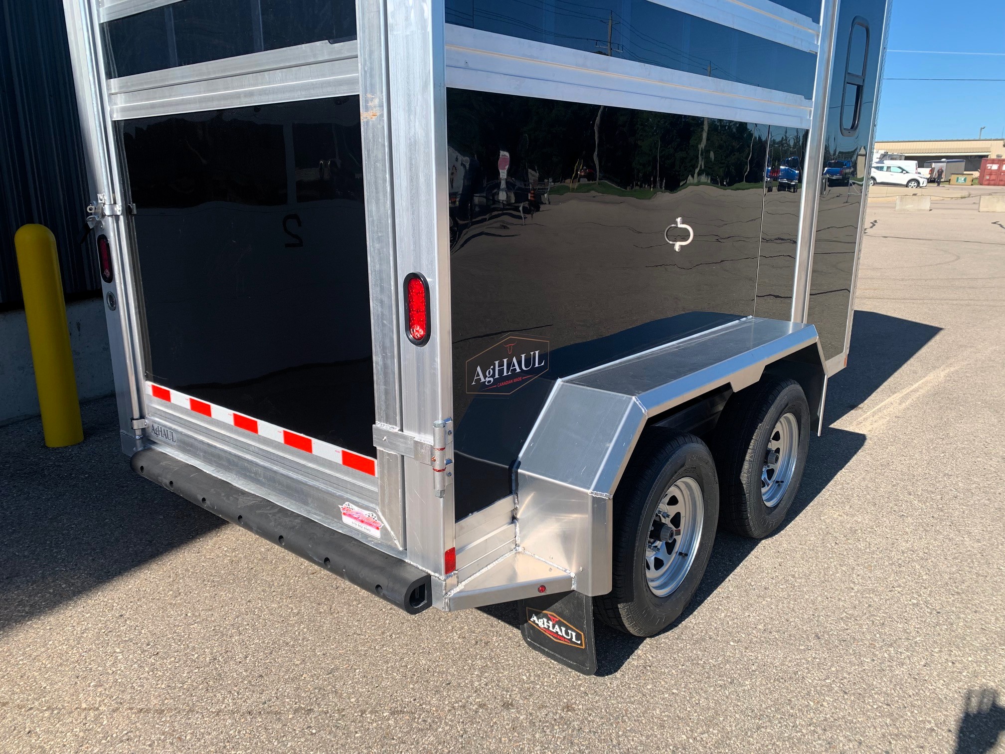 image11 6 - McFarlane Trailer Sales Back view of a shiny aluminum cargo trailer with two rear doors, red taillight, and dual wheels in a parking lot; AgHAUL branding on the bumper tail area.
