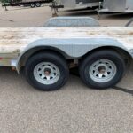 image2 65 - McFarlane Trailer Sales Dual-axle trailer with a weathered wooden deck and curved steel fenders, parked on asphalt with other trailers in the background.