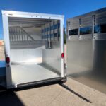 image6 40 - McFarlane Trailer Sales Open aluminum trailer with rear ramp lowered, showing interior divider and ribbed walls against a bright blue sky.
