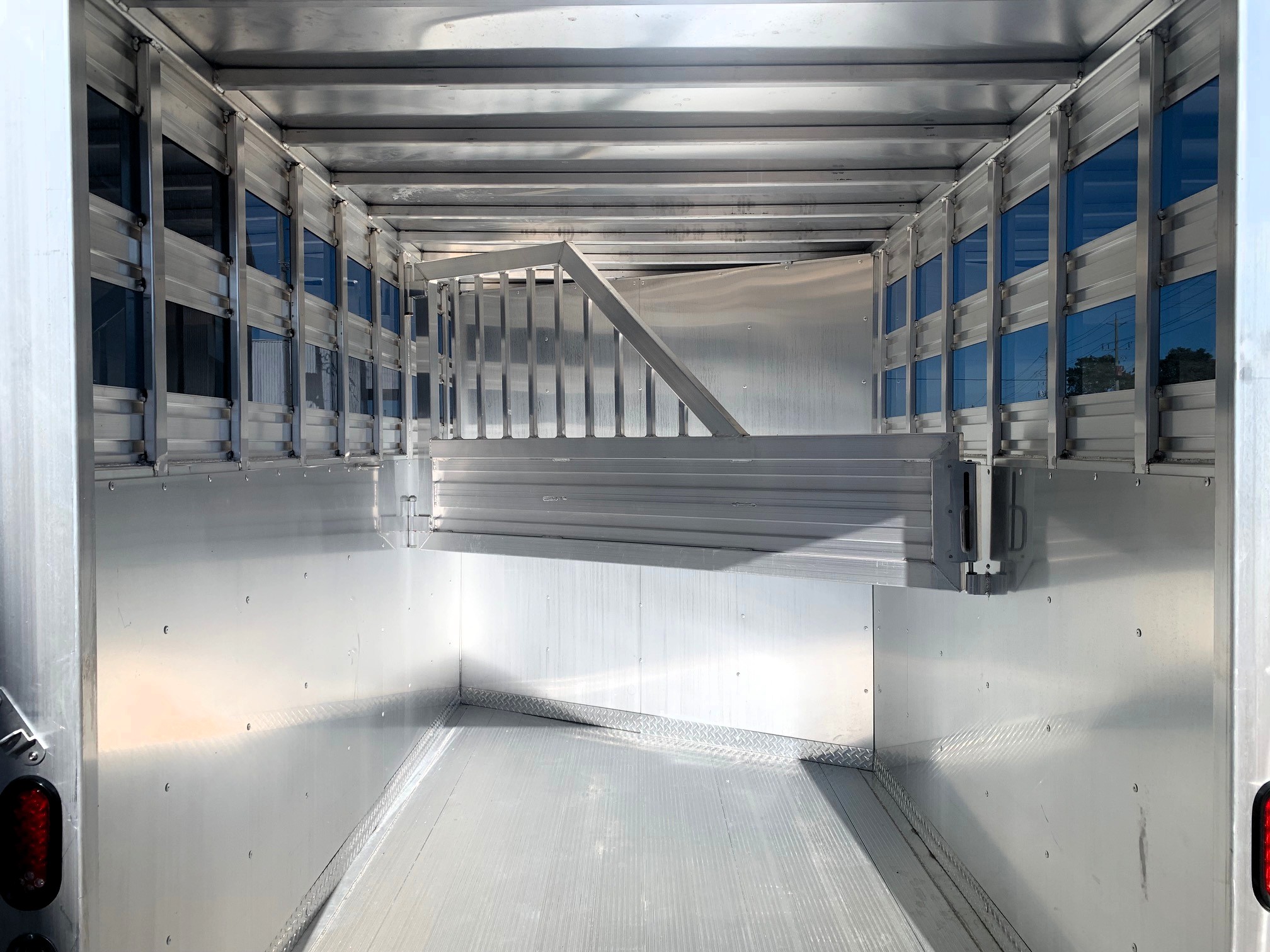 image7 30 - McFarlane Trailer Sales Interior of an empty aluminum trailer with ribbed metal walls and floor, empty cargo area framed by vertical supports.