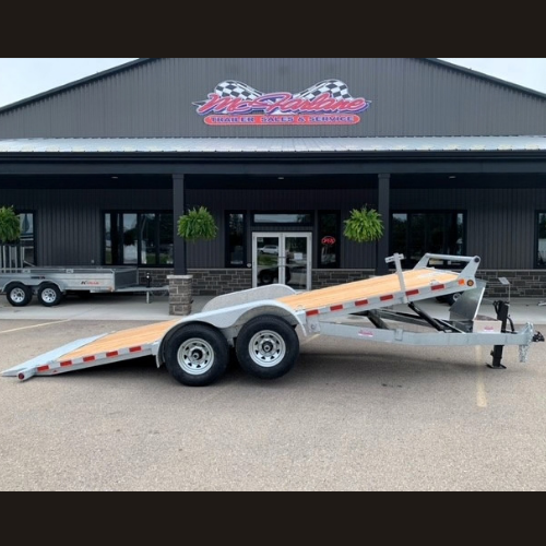Two-axle aluminum car hauler trailer with a raised gooseneck bed and ramps, parked in front of a service shop.